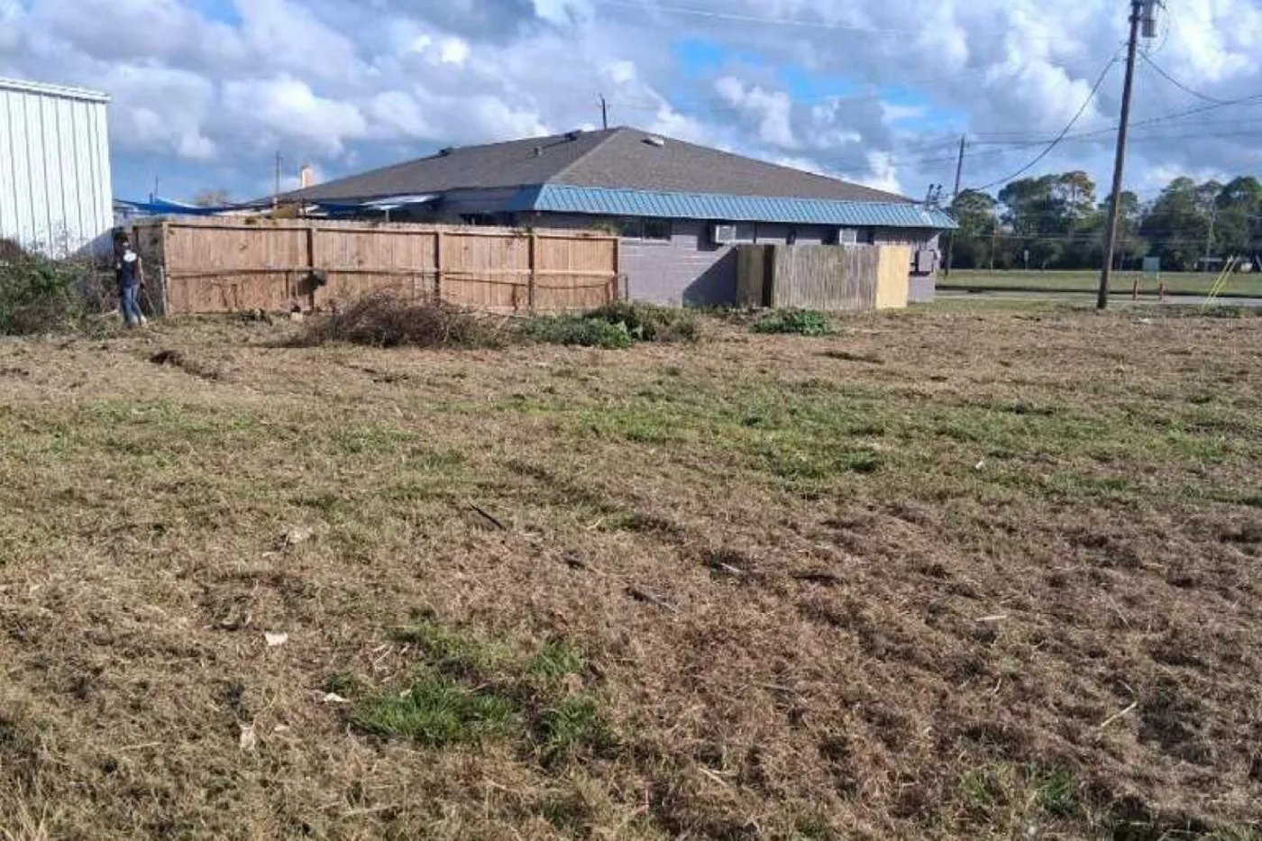 Freshly cleared lot with low brush piles along a wooden privacy fence